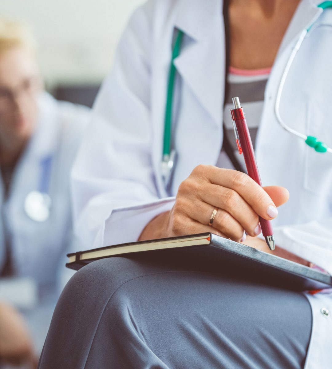 Close up of female medical professional making notes during seminar. Doctor writing notes in diary during healthcare conference.